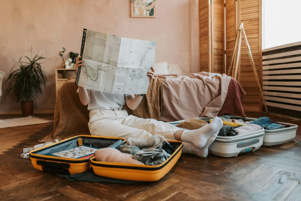 Person packing suitcases with a map in a cozy bedroom, preparing for a journey at Big Sur Cliff-side